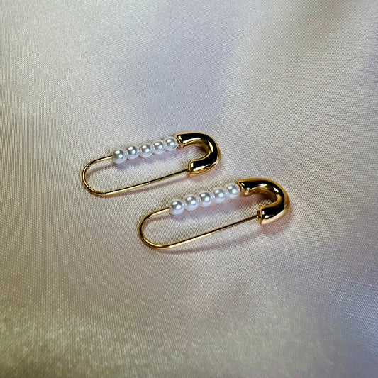 Gold safety pin earrings with pearls on a light fabric background